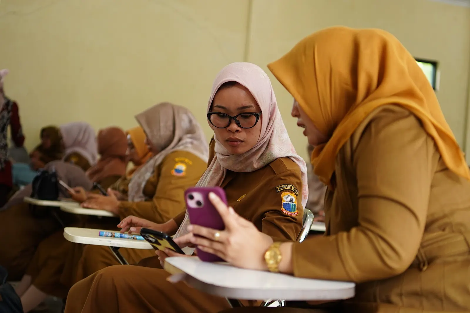 Dua peserta pelatihan membandingkan catatan di ponsel dan buku
