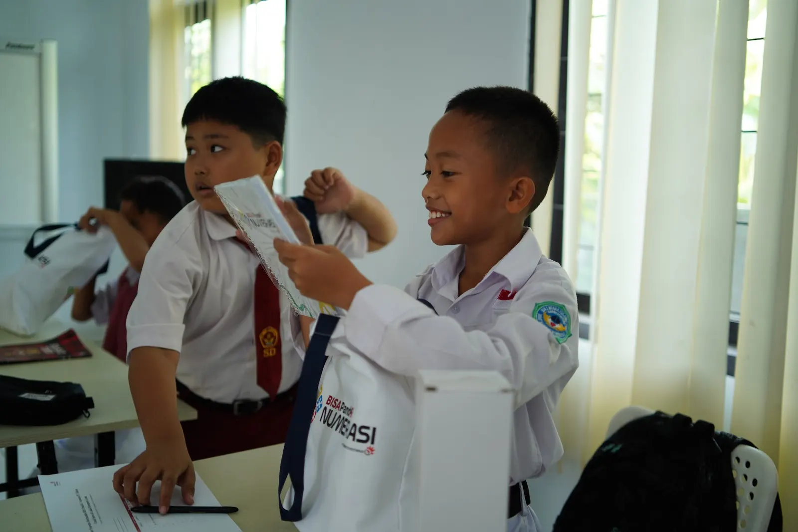 Dua siswa tersenyum sambil membuka tas perlengkapan BISA PandAI Numerasi