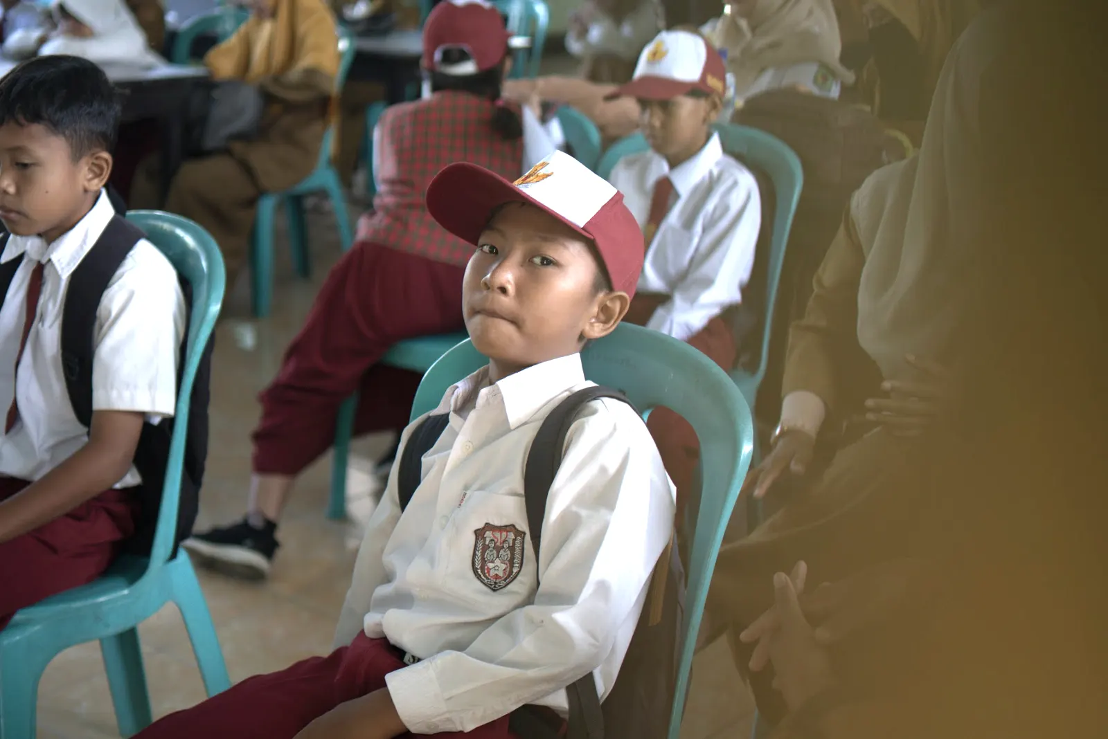 Seorang siswa bertopi merah putih menoleh ke arah pemateri dengan ransel di punggung
