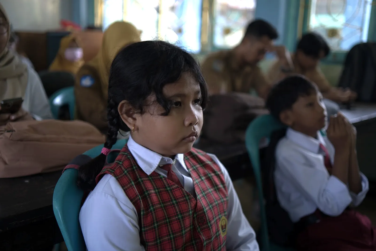 Seorang siswi berseragam kotak-kotak menyimak dengan serius di ruang kelas